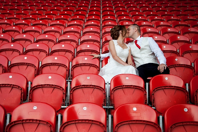 Bride and groom kissing in the red stadium seats at Totally Wicked Stadium