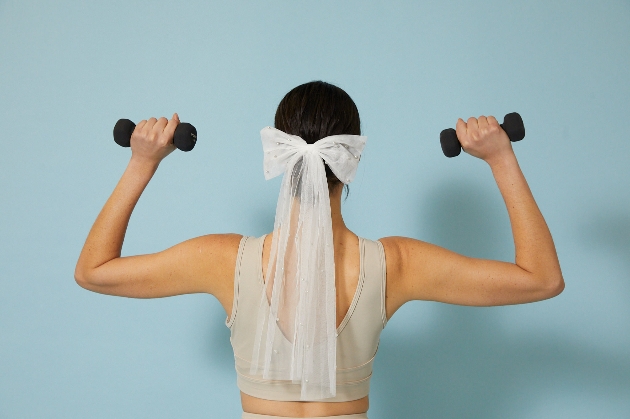 Bride lifting weights wearing bow and veil in her hair