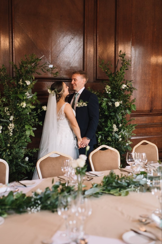 bride and groom behind the top table in front of their floral backdrop